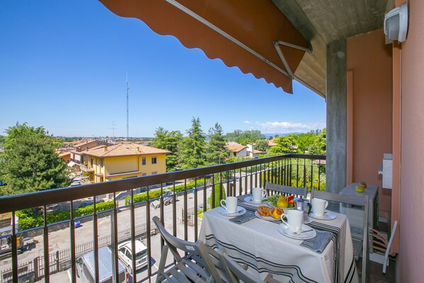 Un balcon avec une table dressée pour le petit-déjeuner, donnant sur un quartier résidentiel avec des maisons et de la verdure.