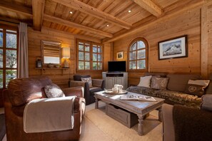A cozy log cabin interior with a leather sofa, a wooden coffee table, and a television.