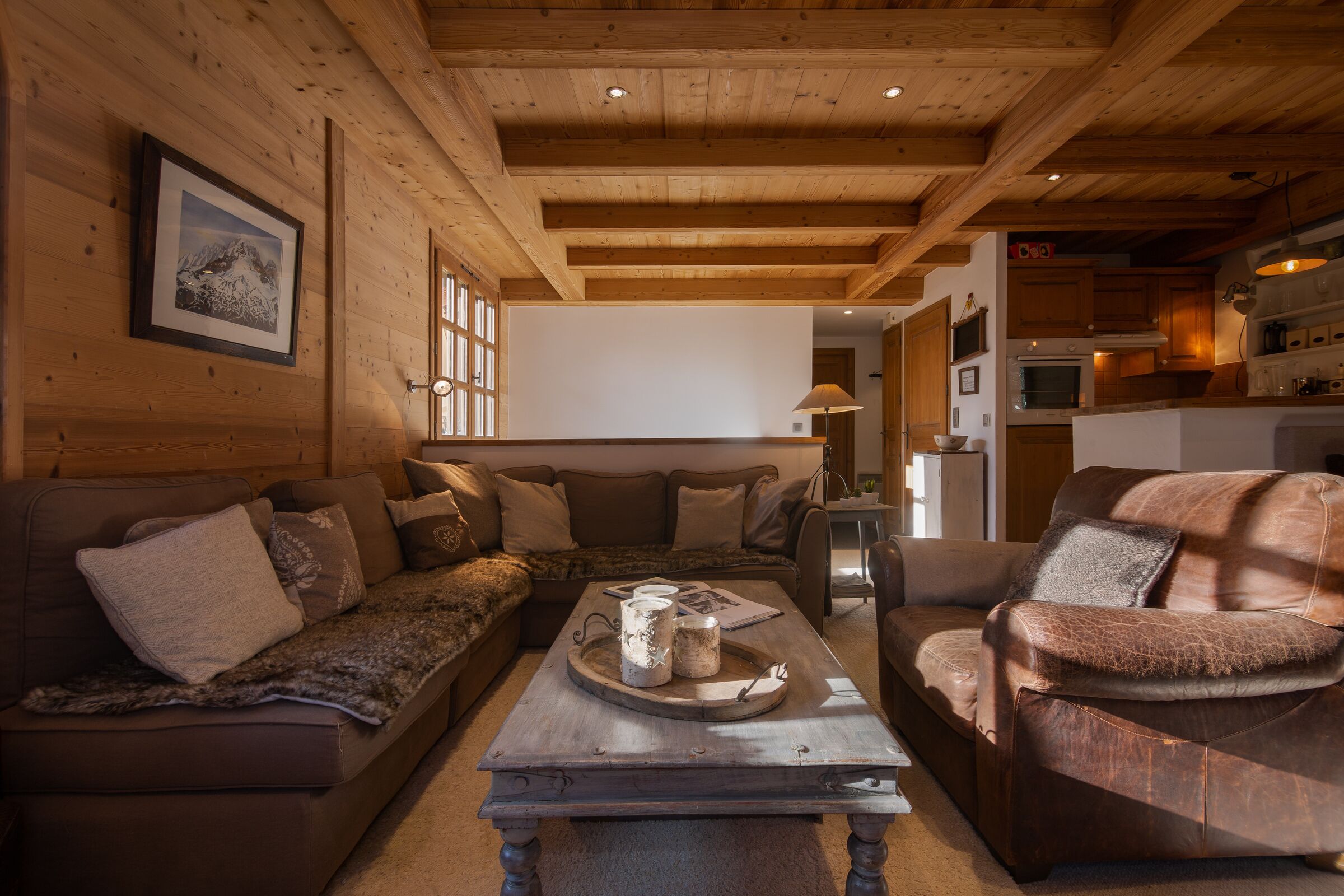 Un salon chaleureux avec des murs et un plafond en bois, un canapé en cuir marron, une table basse en bois agrémentée d’objets décoratifs et un tableau encadré accroché au mur.