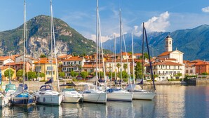 Uma marina com vários veleiros atracados, uma montanha ao fundo e uma cidade com edifícios e uma torre.