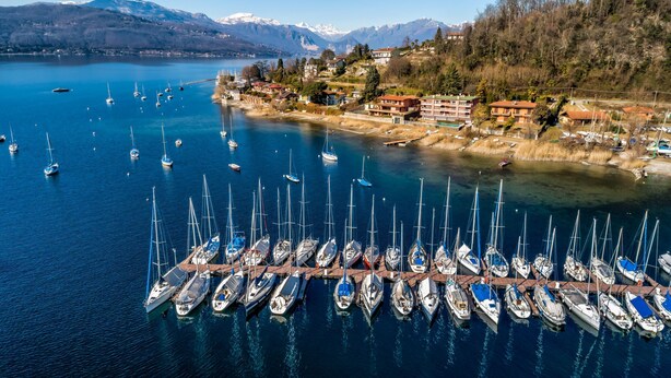 Uma marina com vários veleiros atracados, rodeada por edifícios e montanhas ao fundo.