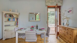 Uma sala de jantar com uma mesa branca, cadeiras listradas, um armário de madeira e uma estante.