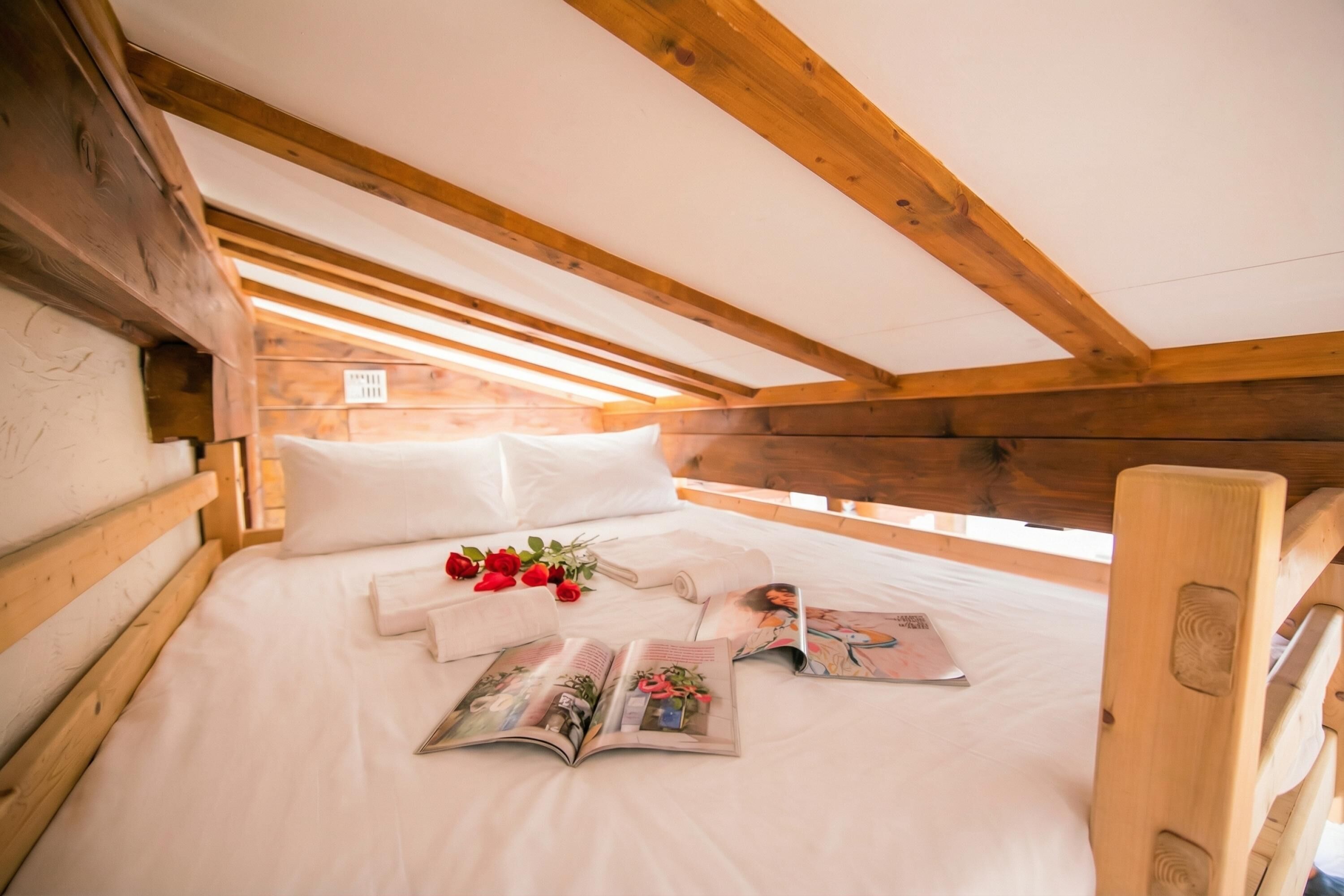Een slaapkamer in de zolder met houten frame, een bed, kussens en een tijdschrift.