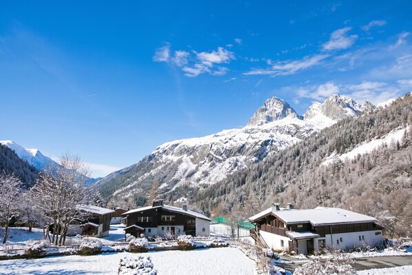 A mountain resort with chalet-style buildings, a clear sky, and snow-covered peaks in the background.