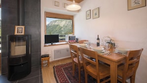 Un coin repas avec une table dressée pour quatre personnes, une cheminée, une fenêtre donnant sur les montagnes et un ventilateur de plafond.