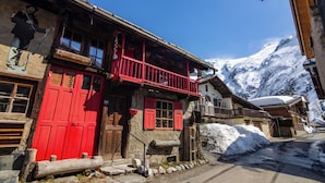 Un bâtiment traditionnel en bois, avec une porte rouge, un balcon et une vue sur les montagnes en arrière-plan.