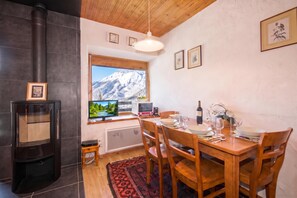 Cozinha acolhedora com fogão a lenha, mesa de jantar posta para quatro pessoas e uma grande janela com vista para as montanhas.
