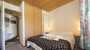 Une chambre à coucher avec un lit, une table de chevet, une lampe, une porte et une fenêtre avec des rideaux.