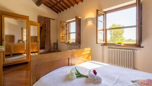 A bedroom with a wooden ceiling, a large mirror, a bed with a white bedspread, and a window with a view of greenery. - Villa Pallina 4BR Villa with Private Pool, Massarosa, Italy (Massarosa)