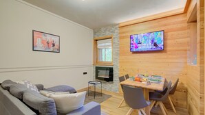 A modern living room with a grey sofa, a dining table with chairs, a TV mounted on the wall, and a fireplace. - Viola, Livigno, Italy (Livigno)