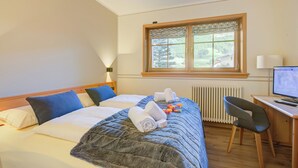 A hotel room with a bed, a desk with a computer, a chair, and a window with a view of greenery. - Viola, Livigno, Italy (Livigno)