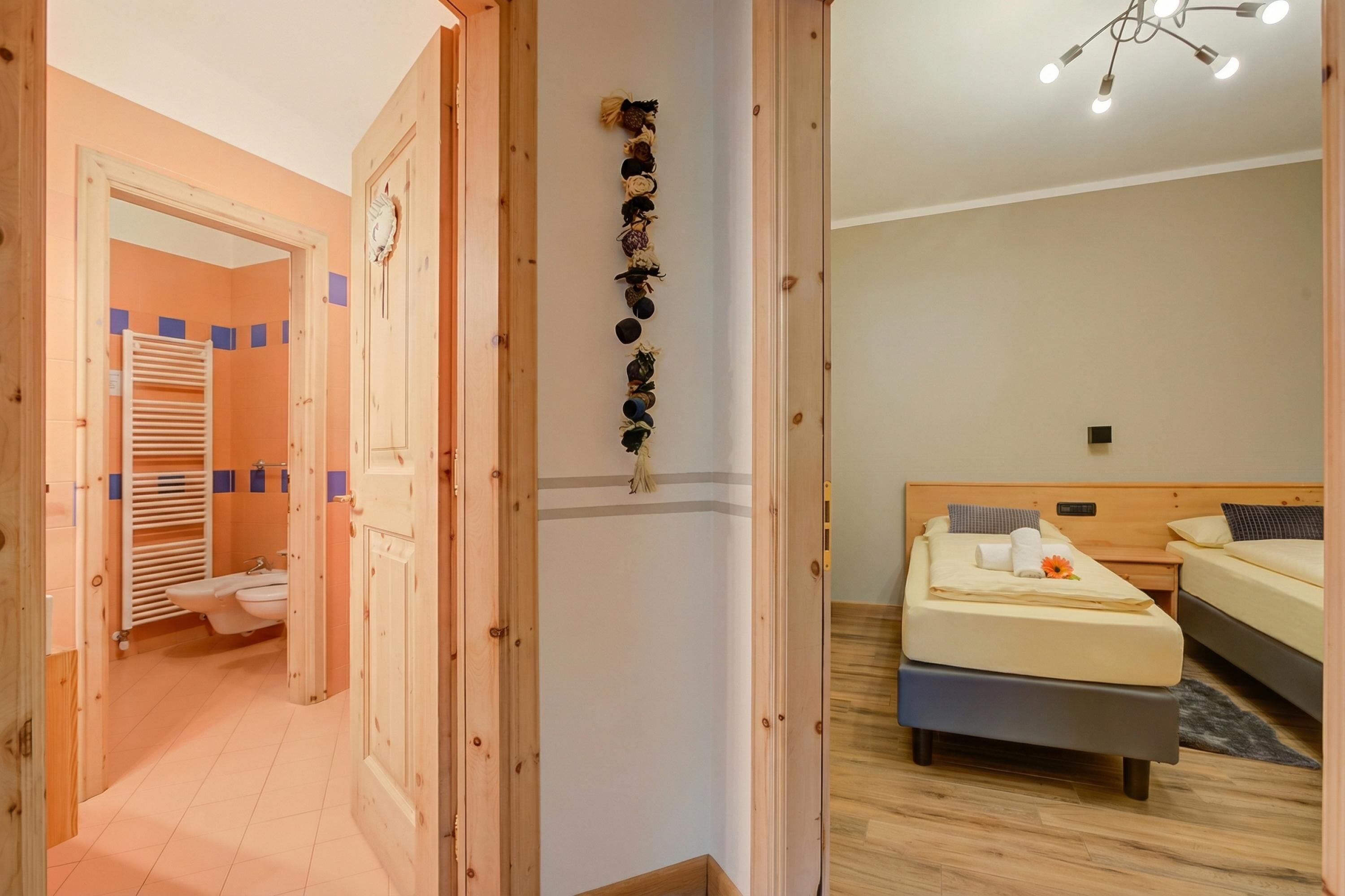 A hotel room with a wooden floor, a bed with a pillow and a flower, a bedside table, and a wall-mounted clock.