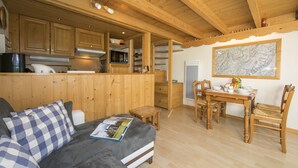 Un accogliente interno di una baita con un letto, un tavolo da pranzo, sedie, armadietti in legno e una mappa appesa al muro.