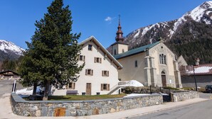 Una chiesa con facciata in pietra, un campanile e una montagna innevata sullo sfondo.