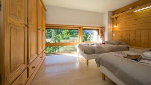 Camera da letto con due letti, un armadio in legno, una grande finestra e vista sul verde.