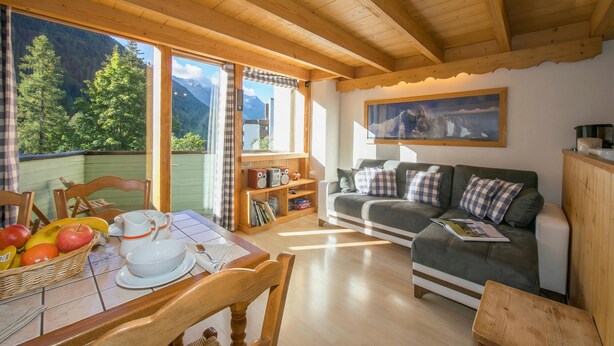 Un interno in legno con un tavolo da pranzo, sedie, un divano e vista sulle montagne attraverso ampie finestre.