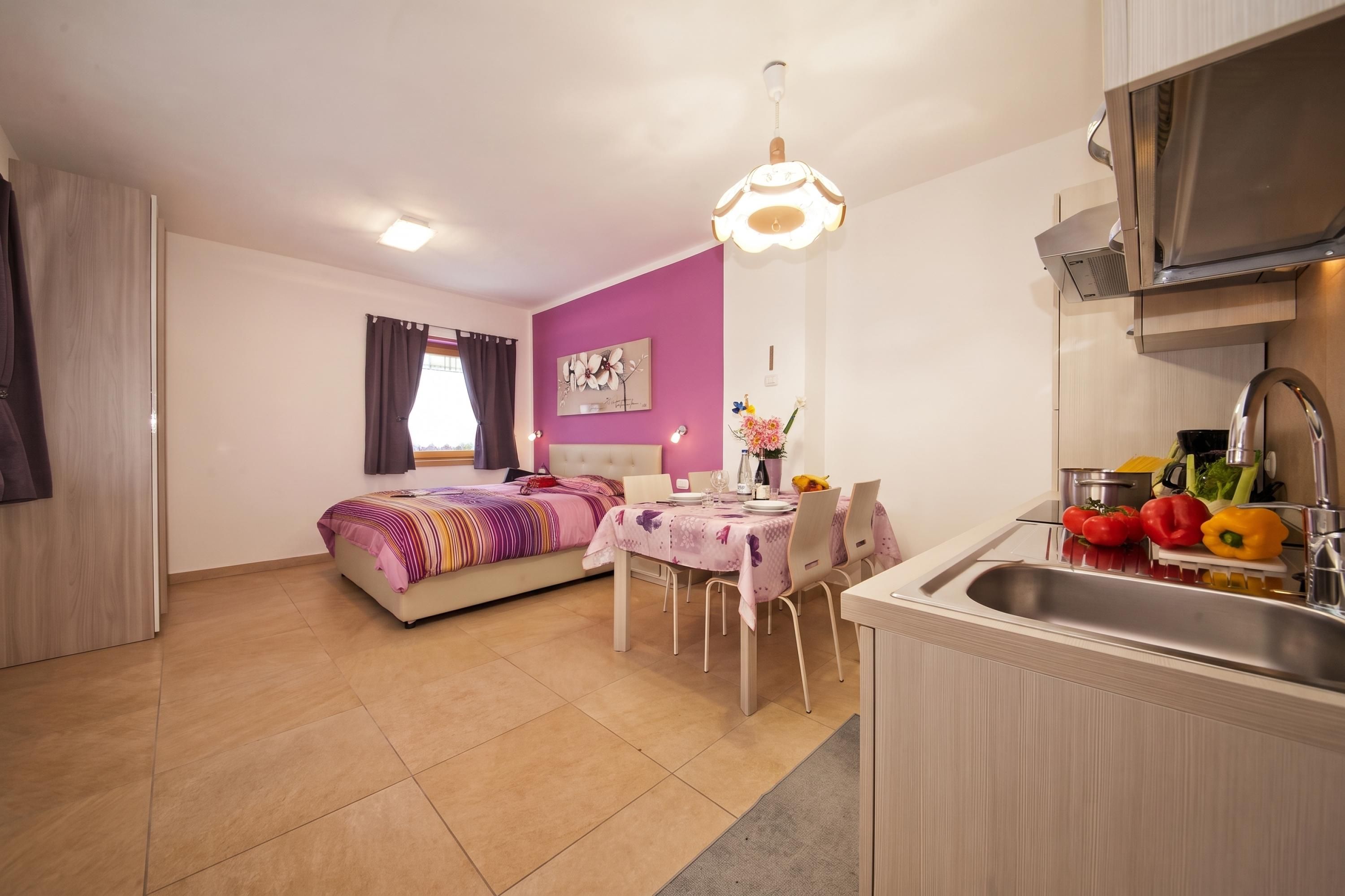 A compact room with a bed, a dining table, and a kitchenette.