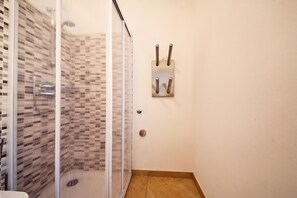 Área de chuveiro com porta de vidro, parede revestida em azulejos e suporte de toalhas de metal fixado na parede.