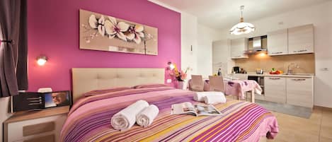 Una habitación de hotel con cama, un cuadro, zona de comedor y cocina.
