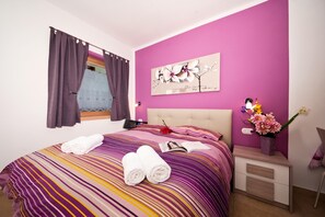 Un dormitorio con cama, una mesita de noche, un florero con flores y un cuadro en la pared.