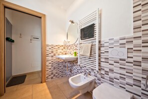 Une salle de bain moderne équipée d’un bidet, d’un lavabo, d’un miroir et d’un porte-serviettes.