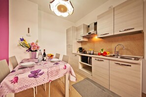Une cuisine moderne avec des meubles en bois, un four encastré et un coin repas agrémenté d’une nappe à motifs floraux.