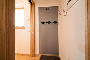 Un couloir avec une porte en bois, un crochet fixé au mur et une petite fenêtre avec un rideau.