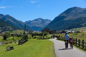 A paved path with cyclists, a wooden fence, and a mountainous backdrop. - Romantico, Livigno, Italy (Livigno)