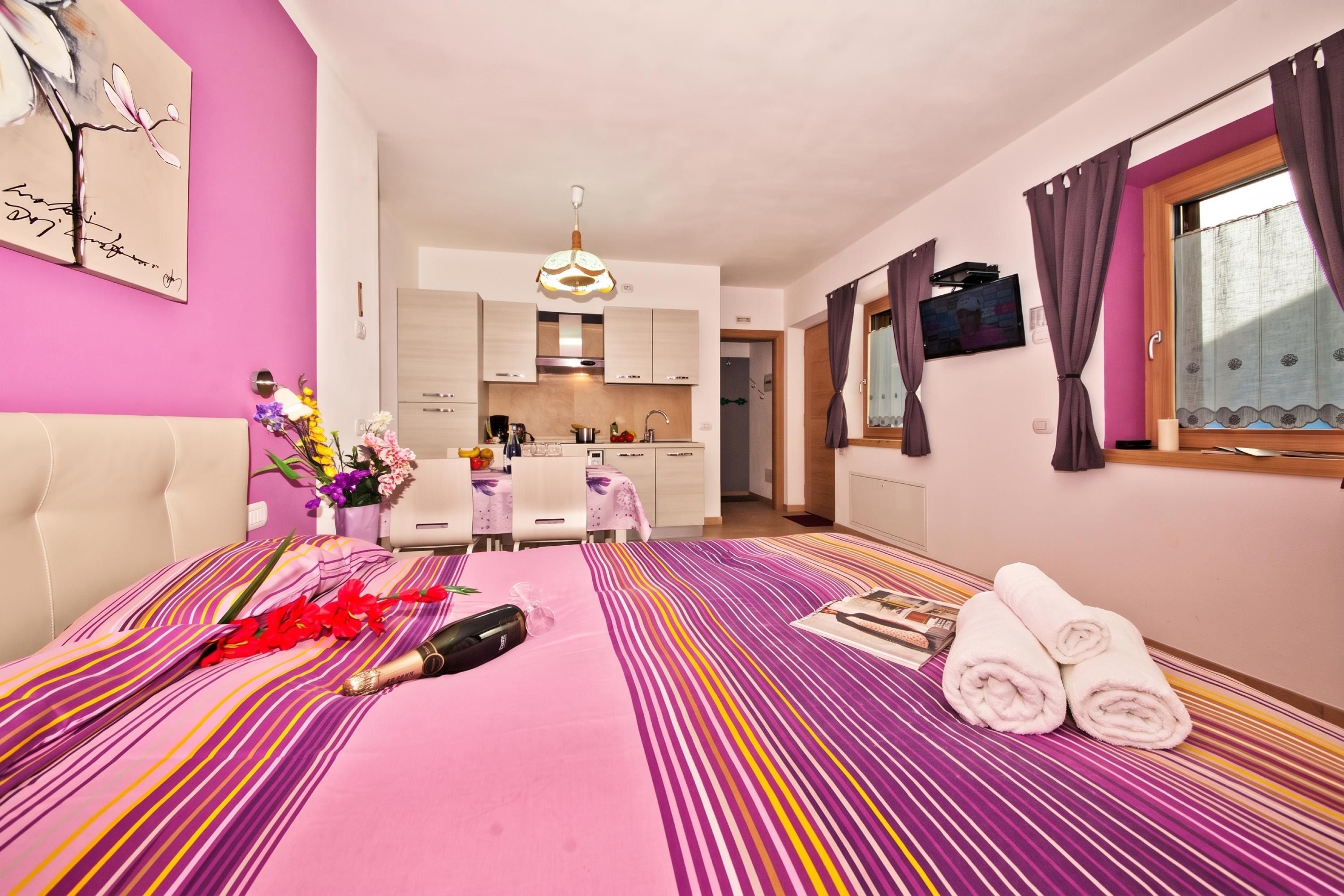 Habitación de hotel con cama, mesa de comedor, zona de cocina y televisor.