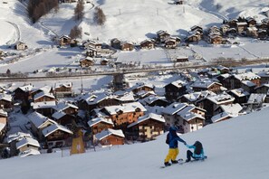 Un village enneigé avec des maisons en bois, une piste de ski et un pont.