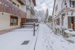 Een besneeuwde buitenruimte met een houten bank en een tafel, omringd door gebouwen met balkons en ramen.