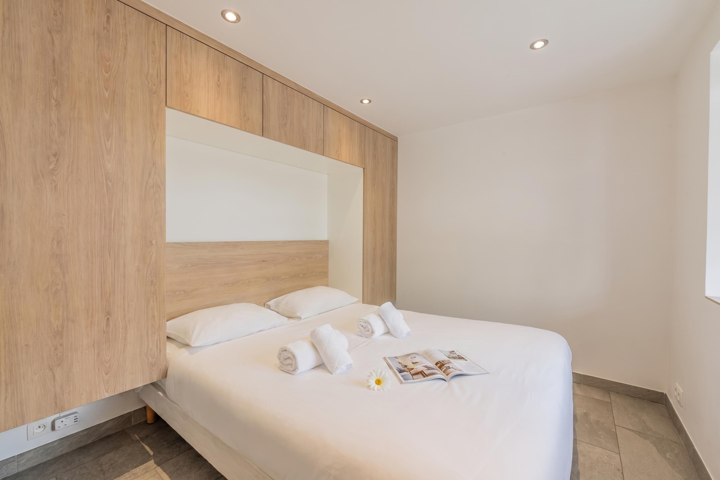 A modern hotel room with a large bed, wooden headboard, and a built-in shelf.