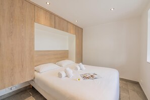 Une chambre d’hôtel moderne avec un grand lit, une tête de lit en bois et une étagère intégrée.