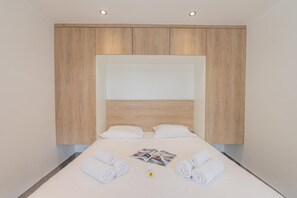 Een hotelkamer met een bed, twee opgerolde handdoeken, een tijdschrift en een klein bloemetje.