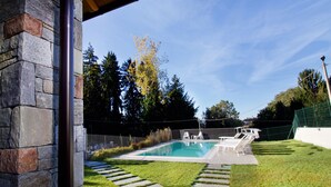 Ein Swimmingpool mit Liegestühlen, umgeben von einer Steinmauer und einer Rasenfläche.
