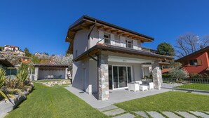 Ein zweistöckiges Haus mit Balkon, einer Terrasse und Gartenmöbeln sowie einem gepflegten Rasen.