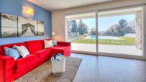 Ein modernes Wohnzimmer mit einem roten Sofa, einem Couchtisch und einer großen Schiebeglastür, die zu einem Hinterhof mit Pool führt.
