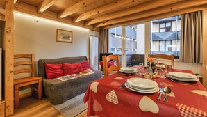 A cozy room with a wooden ceiling, a sofa with red cushions, a dining table set with plates and cutlery, and a window with curtains. - Grand Roc C122 280m from Slopes & Parking, Argentière (Chamonix), France (Argentière (Chamonix))