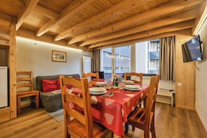 Un comedor con una mesa dispuesta para cuatro personas, sillas de madera, mantel rojo y un televisor montado en la pared.