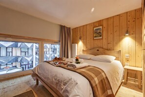 A bedroom with a large bed, wooden walls, a window with a view of buildings, and a painting on the wall. - Grand Roc C122 280m from Slopes & Parking, Argentière (Chamonix), France (Argentière (Chamonix))