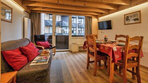 A cozy room with a wooden ceiling, a sofa with red cushions, a dining table set for two, and a large window with curtains. - Grand Roc C122 280m from Slopes & Parking, Argentière (Chamonix), France (Argentière (Chamonix))