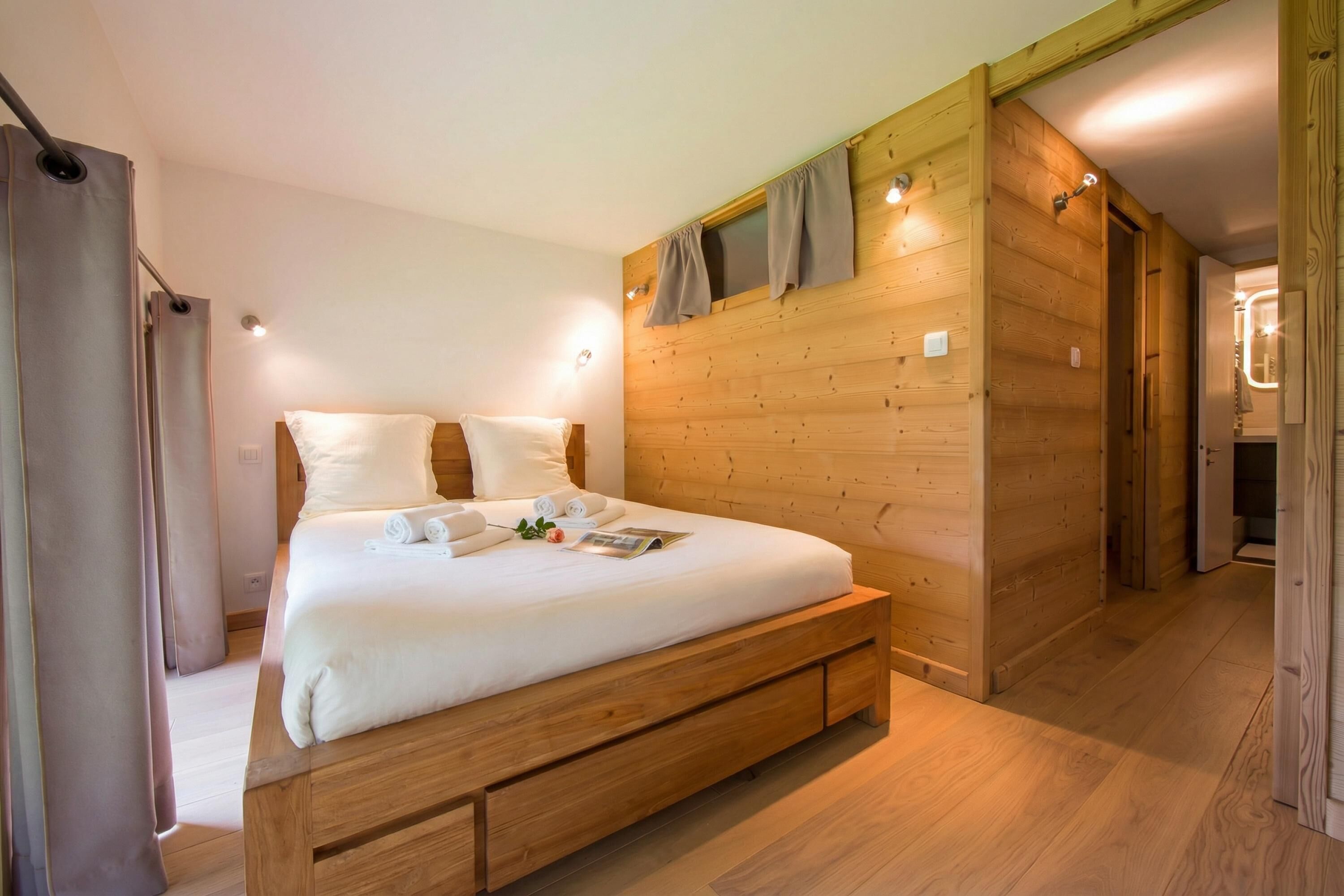 Een slaapkamer met houten lambrisering, een bed, gordijnen en een houten deur.