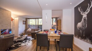 Un soggiorno moderno con televisione, angolo pranzo con tavolo e sedie, e un grande quadro raffigurante un cervo appeso al muro.