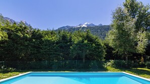 Una piscina rettangolare con superficie d'acqua blu trasparente, circondata da una recinzione verde e alberi, con una catena montuosa sullo sfondo.