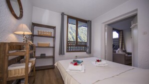 Una camera da letto con un letto, una mensola in legno con cesti, una finestra vista e una porta che conduce a un'altra stanza.