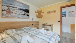 A hotel room with a large bed, a wooden headboard, a painting of a snowy landscape, a small table with a lamp, and a wooden wall decoration. - Italia 1 Ski in- Ski out 50m, Livigno, Italy (Livigno)