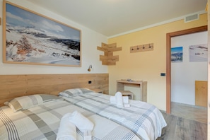 A hotel room with a large bed, a wooden headboard, a painting of a snowy landscape, a small table with a lamp, and a wooden wall decoration.