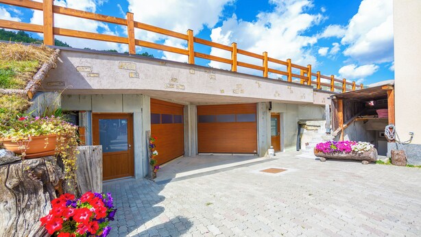 A building with a wooden deck, a garage, and flower planters. - Italia 1 Ski in- Ski out 50m, Livigno, Italy (Livigno)