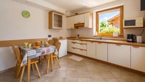 A kitchen with a dining table, chairs, cabinets, a window with a view, and a clock on the wall. - Italia 1 Ski in- Ski out 50m, Livigno, Italy (Livigno)