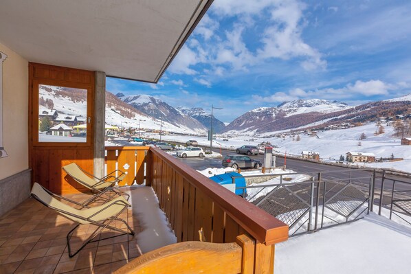 A balcony with a view of a snowy mountain landscape, a wooden railing, and a pair of lounge chairs. - Camoscio Ski in - Ski out 200m, Livigno, Italy (Livigno)